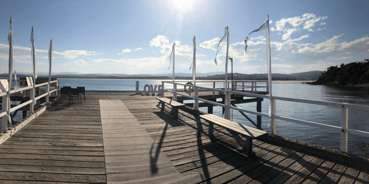 Wooden dock extending over a body of water Merimbula Wharf with 'LOVE' spelled out in flags.