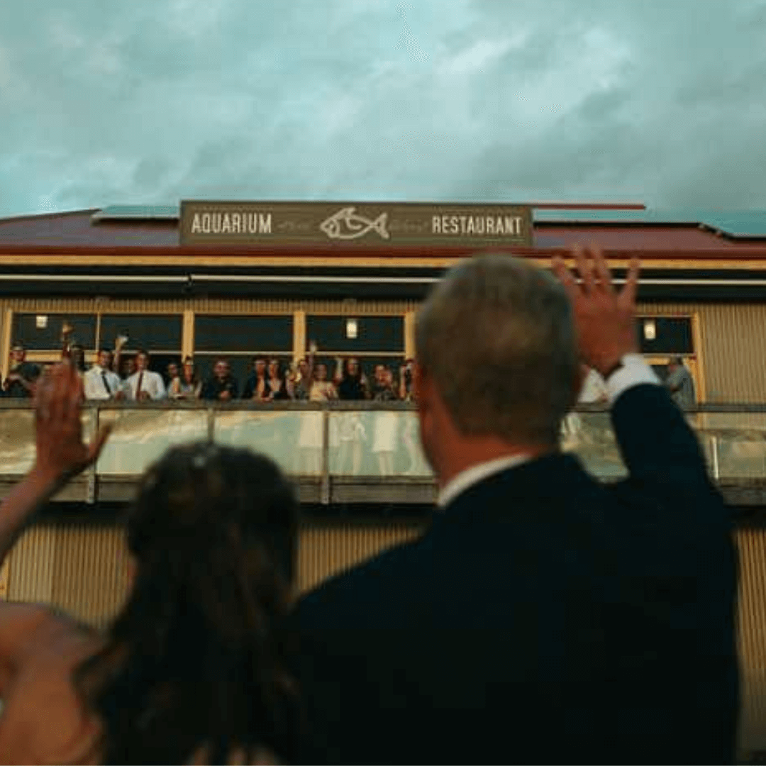 People waving from a balcony overlooking an aquarium restaurant.