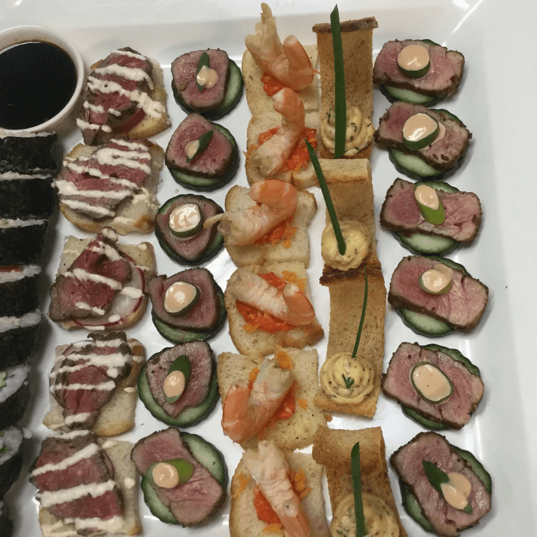 Assorted canapés on a white plate with a side of black and white condiment.