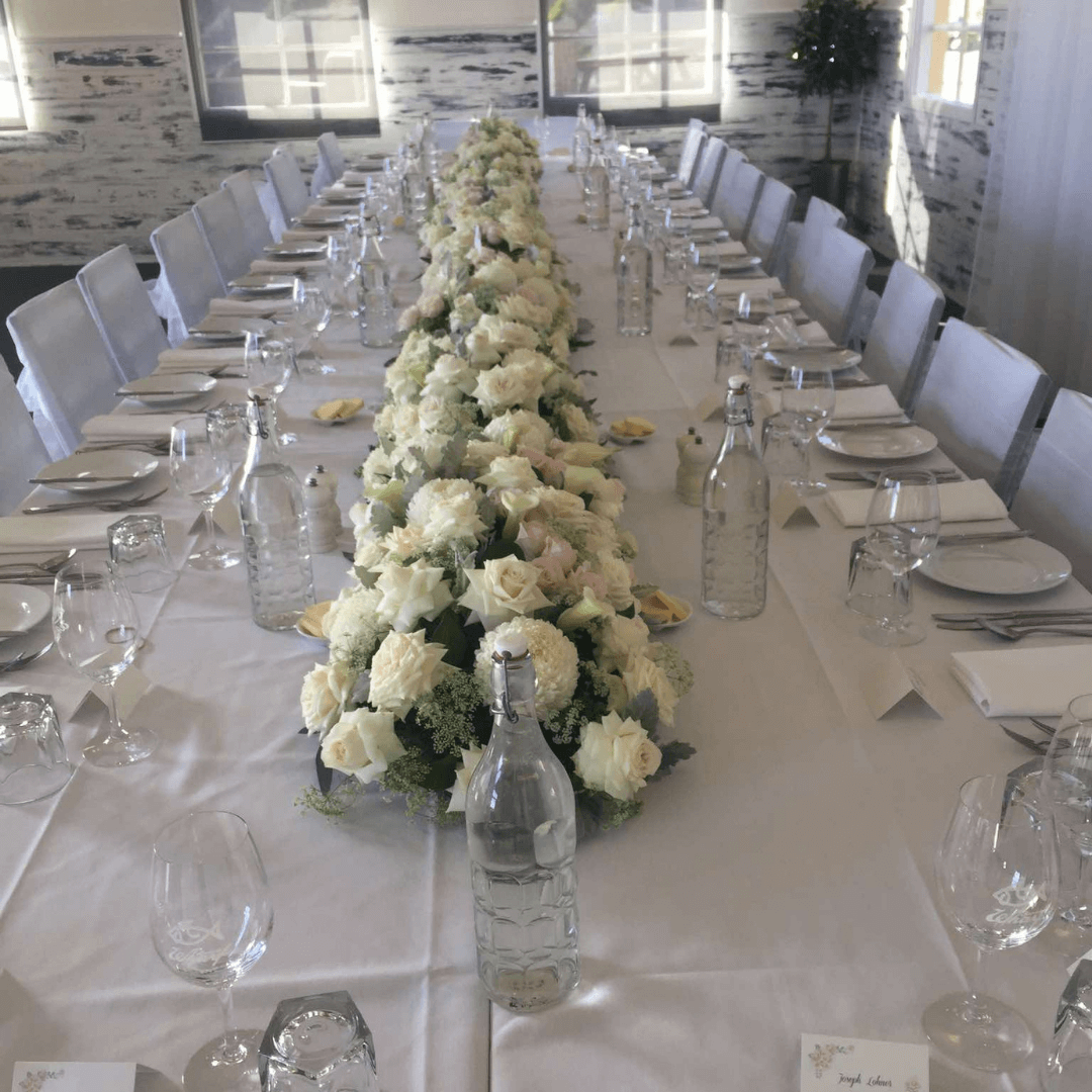 Long dining table set for a formal event with white floral centerpiece, water bottles, and silverware.