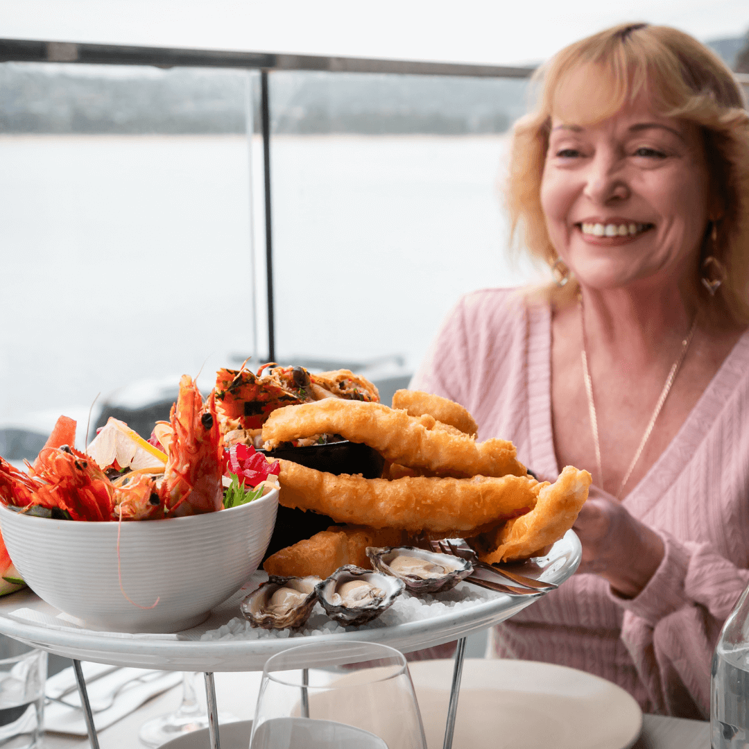 Woman sitting at a table with a seafood platter by a waterfront. Merimbula  Restaurant